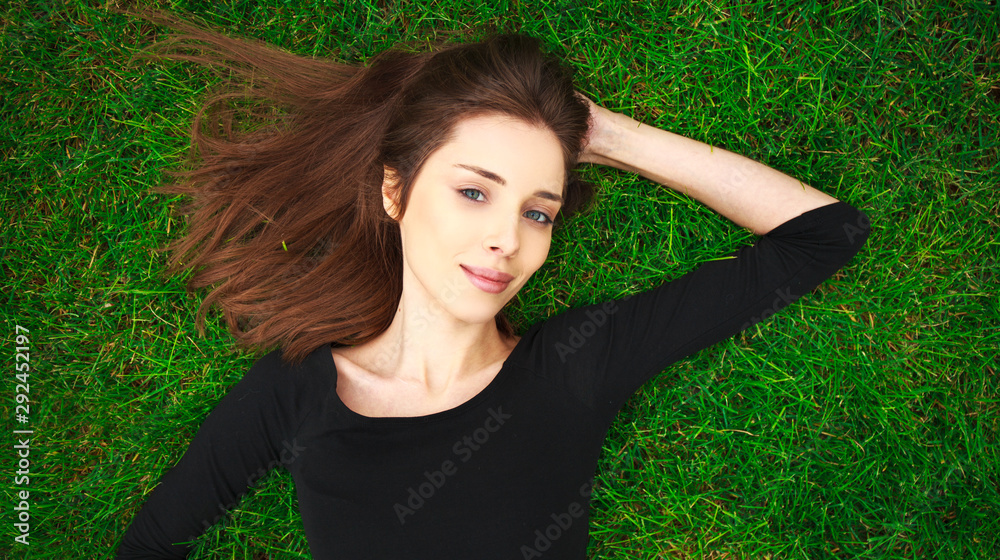 Top view portrait of a young beautiful woman in black dress lies on green lawn in a park Top view portrait of a young beautiful woman in black dress lies on green lawn in a park