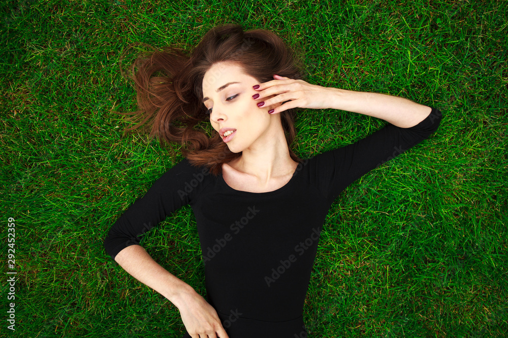 Top view portrait of a young beautiful woman in black dress lies on green lawn in a park Top view portrait of a young beautiful woman in black dress lies on green lawn in a park