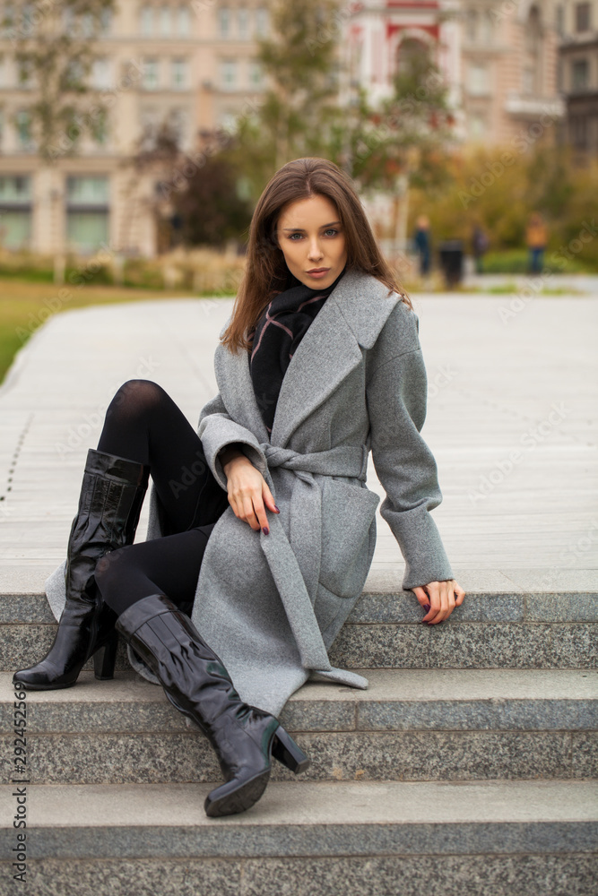 Fototapeta premium Portrait of a young beautiful woman in a black dress sitting on the stone steps in the autumn park