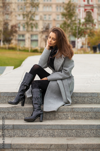 Portrait of a young beautiful woman in a black dress sitting on the stone steps in the autumn park