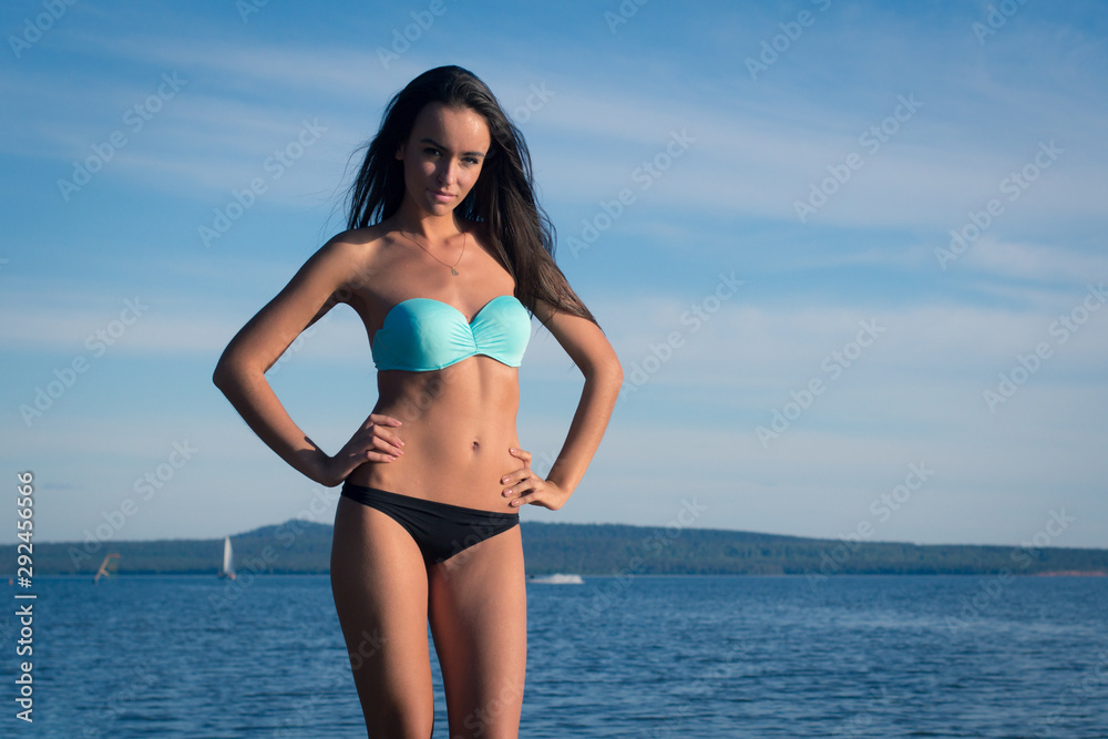 Young woman in a turquoise swimsuit near the water sunbathing on the beach