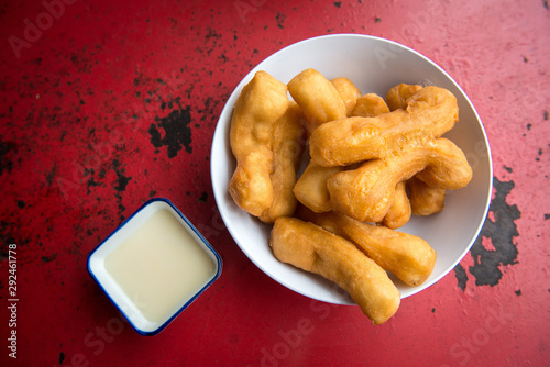 Patongo (or Chinese Doughnut)with condensed milk on the red table. This is very popular breakfast menu in Thailand, dipping with condensed milk or hot coffee is a great choices. photo