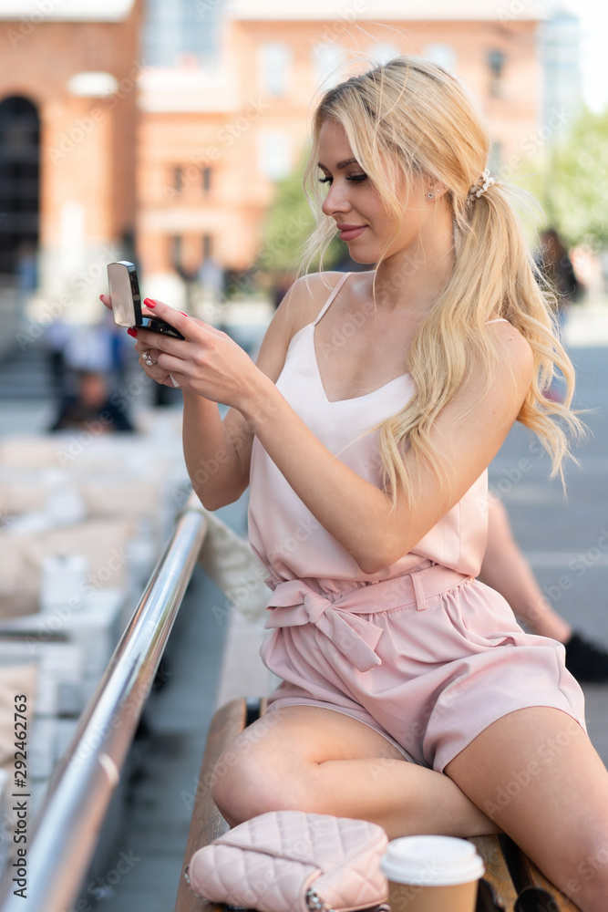 beautiful european blonde girl paints her lips while sitting in street cafe on summer day