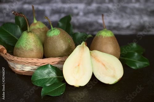 ripe fresh organic pears in a wicker basket and on the table close-up. pears with leaves and halves of pears.