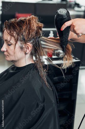 Hairdresser styling dyeing combing womans hair. Young woman working as a hairdresser in hair salon. Real people, authentic situations