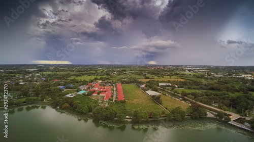 Aerial view above the lake  village and green rice fields plantations  view of heavy raining and storm with dark clouds moving in the sky background  Krajub Reservoir  Ban Pong  Ratchaburi  Thailand.