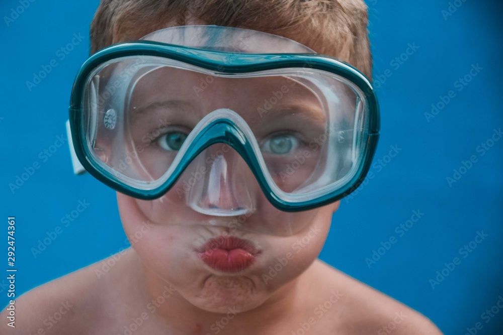 Kid with blue eyes blowing air wearing swimming glasses