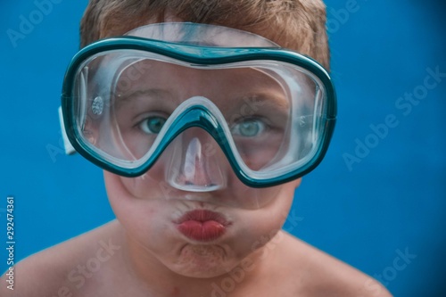 Kid with blue eyes blowing air wearing swimming glasses