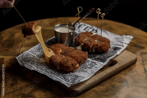 Delicious melting pieces of cheese, sauce, wooden table. Dark underexposed image.
