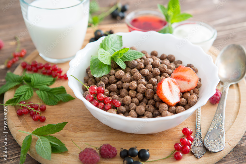 Cereal chocolate balls in bowl with milk on rustic wooden table Healthy tasty breakfast chocolate balls with strawberries, raspberries, black currants and red currants. Cereal chocolate balls in bowl with milk on rustic wooden table Healthy tasty breakfast chocolate balls with strawberries, raspberries, black currants and red currants.