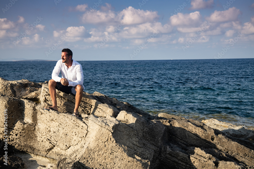 man sitting on the rocks looking at the sea, on vacation at an ibiza beach