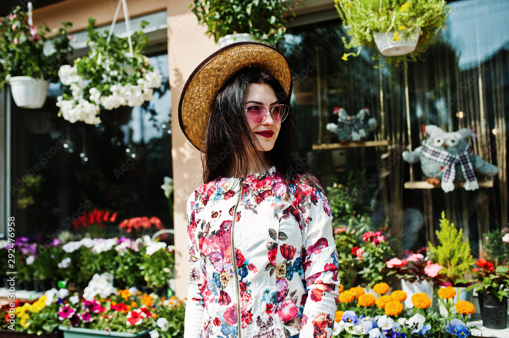 Summer portrait of brunette girl in pink glasses and hat against flowers shop.