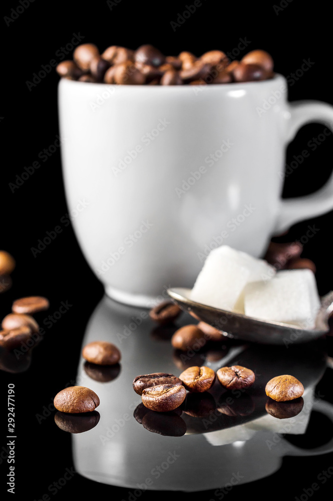 Fototapeta premium Full cup of coffee beans and spoon with sugar cubes on black.