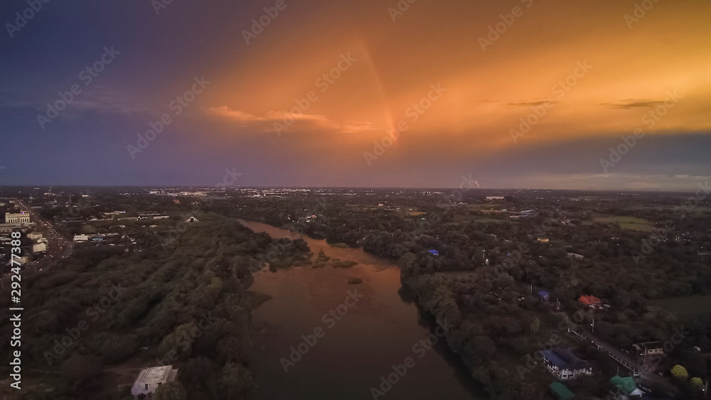 Aerial view sunset above Mae Klong River around with green forest on both bank with yellow sun light and rainbow in cloudy sky background, Ban Pong, Ratchaburi, Thailand.