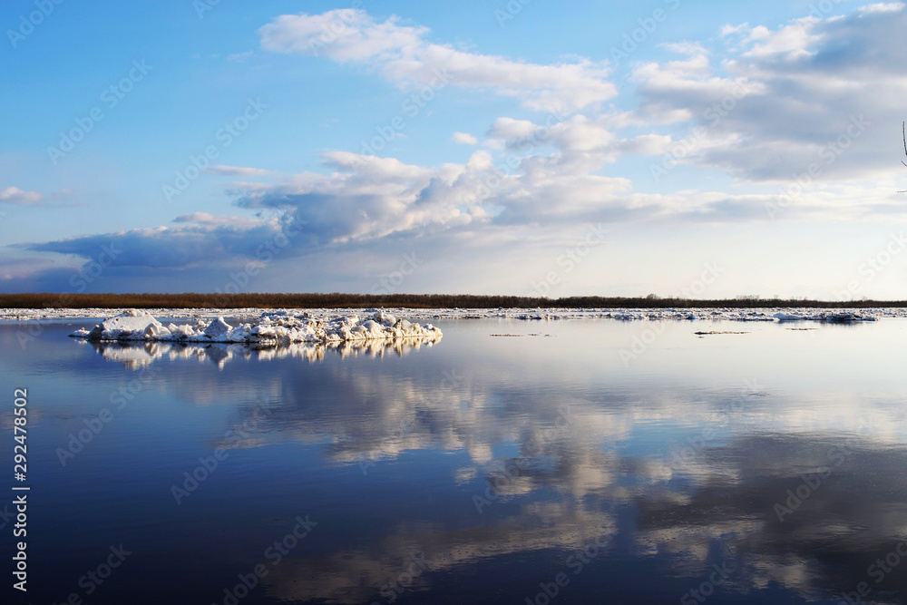 Spring river landscape with ice drift, blue cloudy sky and reflections in the water. Season nature background