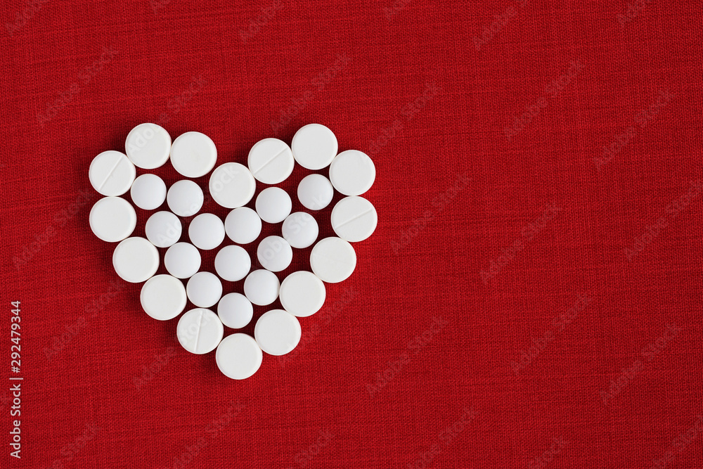 White circle tablet pills of different size placed in form of heart on a dark red fabric background. Heart care concept. Top view. Copy space White circle tablet pills of different size placed in form of heart on a dark red fabric background. Heart care concept. Top view. Copy space