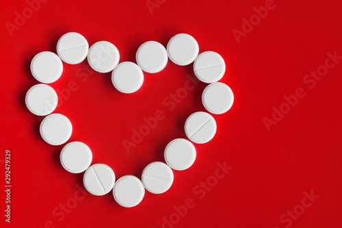 White circle tablet pills placed in form of a heart on a red background. Top view. Copy space photo