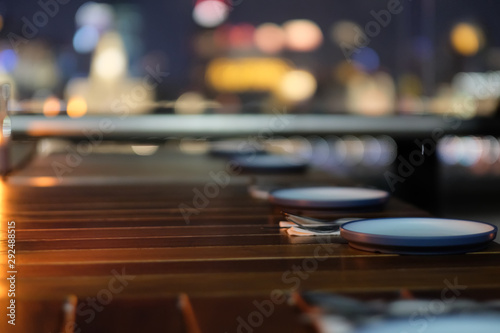 close up plates and cutlery in a row on outdoor restaurant table at night. Blur colorful city lights background.