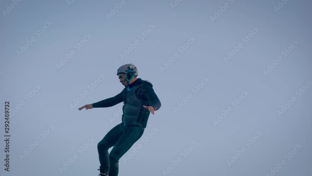 sportsman is practicing flyboarding on water, training tricks, whirling at air, pushing by water flows