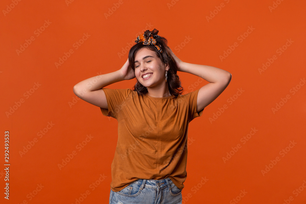 Smiling brunette woman in a t-shirt and beautiful headband standing isolated over orange background. Place for ad. Smiling brunette woman in a t-shirt and beautiful headband standing isolated over orange background. Place for ad.