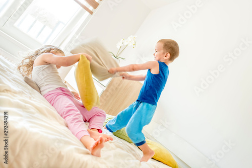 Small children having fun while fighting with pillows in the bedroom and jumping on bed