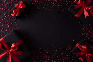 Top view of black christmas boxes with red ribbon on black background with copy space for text. black Friday composition.