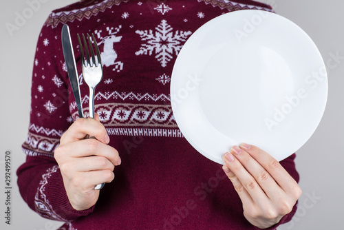 Cropped close up photo of hands showing silver cutlery and white round plate in hands isolated grey color background