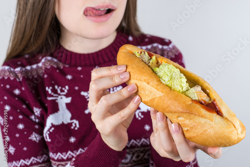 Cropped close up photo portrait of happy smiling satisfied tongue-out girl holding long big burger in hands preparing for biting isolated grey color background