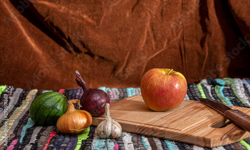 A small watermelon  onion  garlic  Apple and a chopping Board with a knife on a table covered with a handmade tablecloth