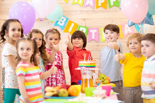 Children celebrating birthday party. Kids stand arround festive table and show thumbs up