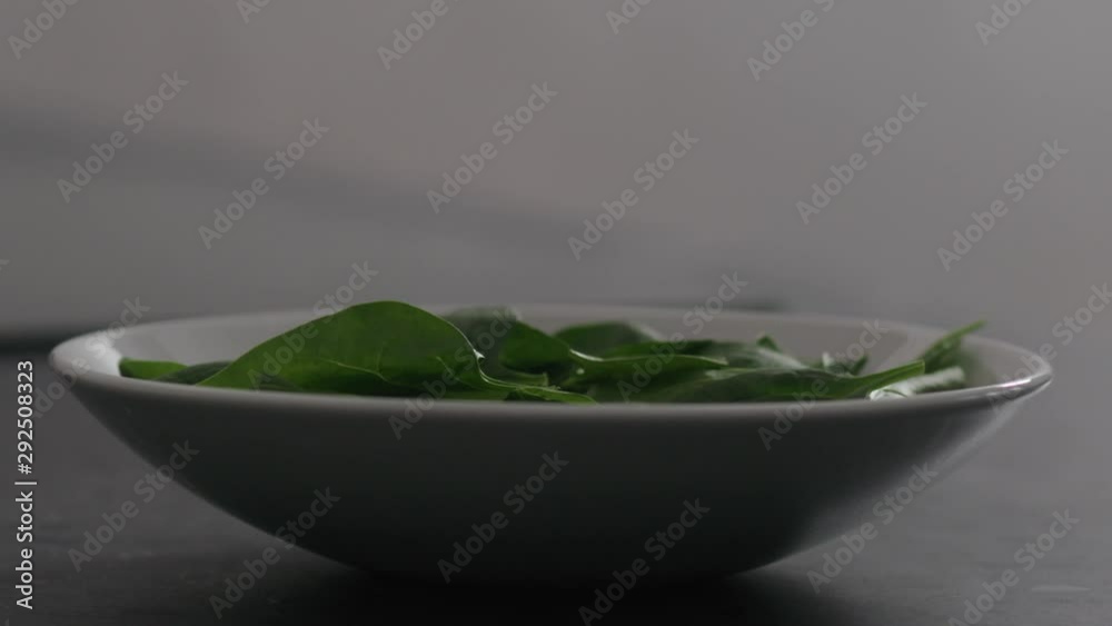 Slow motion fresh spinach leaves falling into bowl on kitchen countertop Slow motion fresh spinach leaves falling into bowl on kitchen countertop