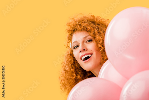 cheerful redhead woman with pink balloons isolated on yellow © LIGHTFIELD STUDIOS