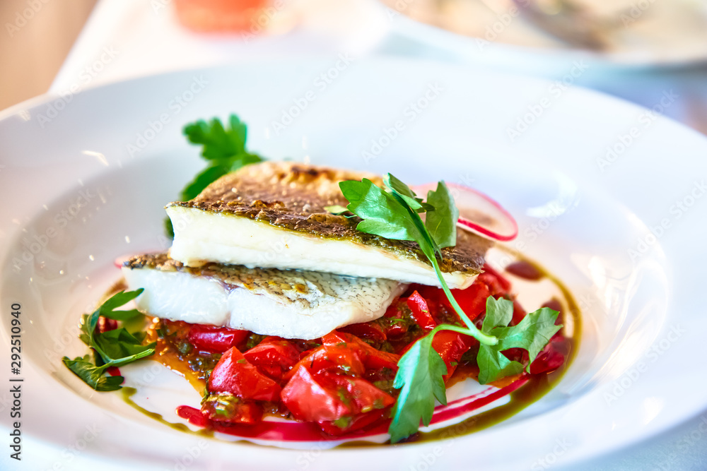 Fried fish fillet with tomatoes lie on a plate in a restaurant