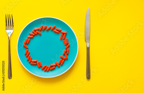 Colorful Capsules On A Plate With Fork And Knife On A Yellow Background with copy space. photo