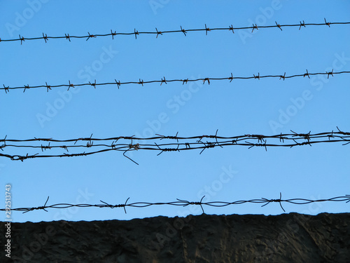 Several threads of old rusty barbed wire, hand- made, stretched over an old concrete fence on a clear blue sky background close-up photo