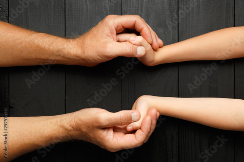 Hands of an elderly man holding the hand of a younger man.