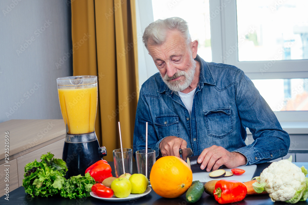 Elderly man making fresh vitamin juices smoothies and cut zucchini with a knife on the board bid window background Elderly man making fresh vitamin juices smoothies and cut zucchini with a knife on the board bid window background