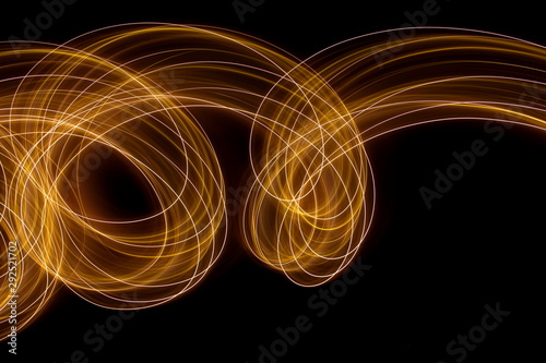 Long exposure photograph of metallic gold neon colour in an abstract swirl, parallel lines pattern against a black background. Light painting photography. photo