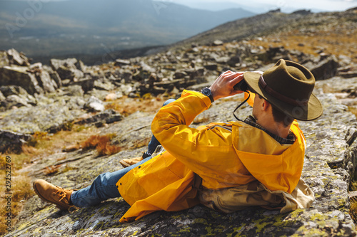 young hiker having a rest on mountains looking through binocular at the distance, close up back view photo.