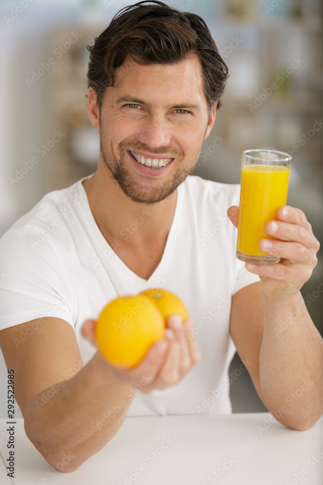 handsome man holding glass of juice and fresh oranges