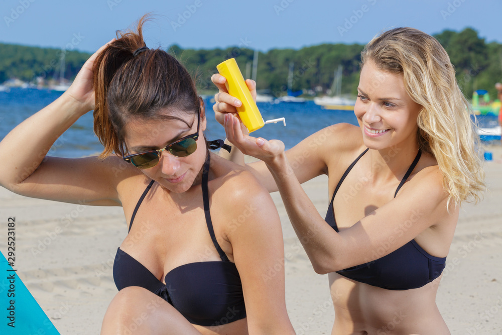 woman applying suncream to her friends back woman applying suncream to her friends back