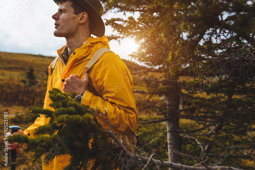 handsome tourist enjoying the smell of fresh air, standing net to fur tree. close up side view photo, sunset