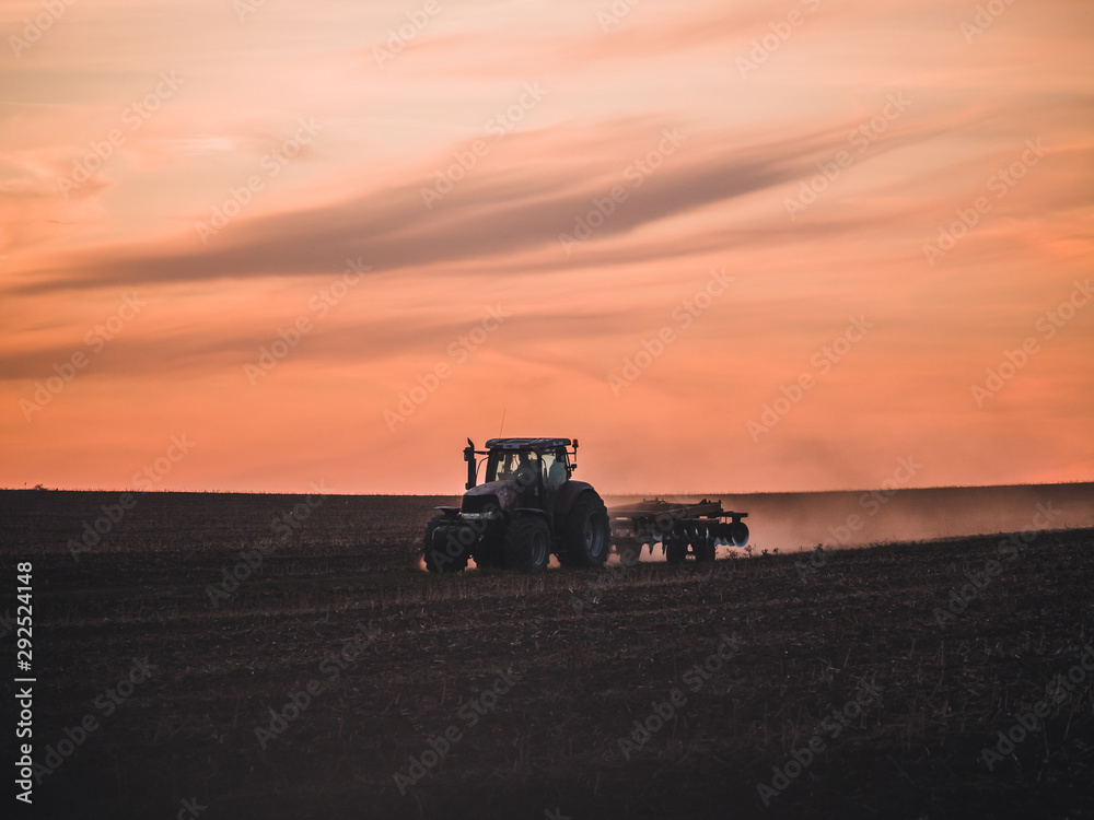 Fototapeta premium Tractor on filed by sunset.