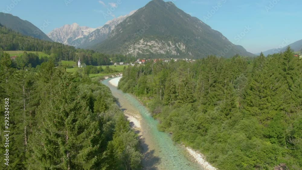 DRONE Gorgeous emerald stream runs through the scenic countryside under the Julian Alps. Picturesque flying view of a mountain stream as it cascades past pastures and woods and towards a quiet village