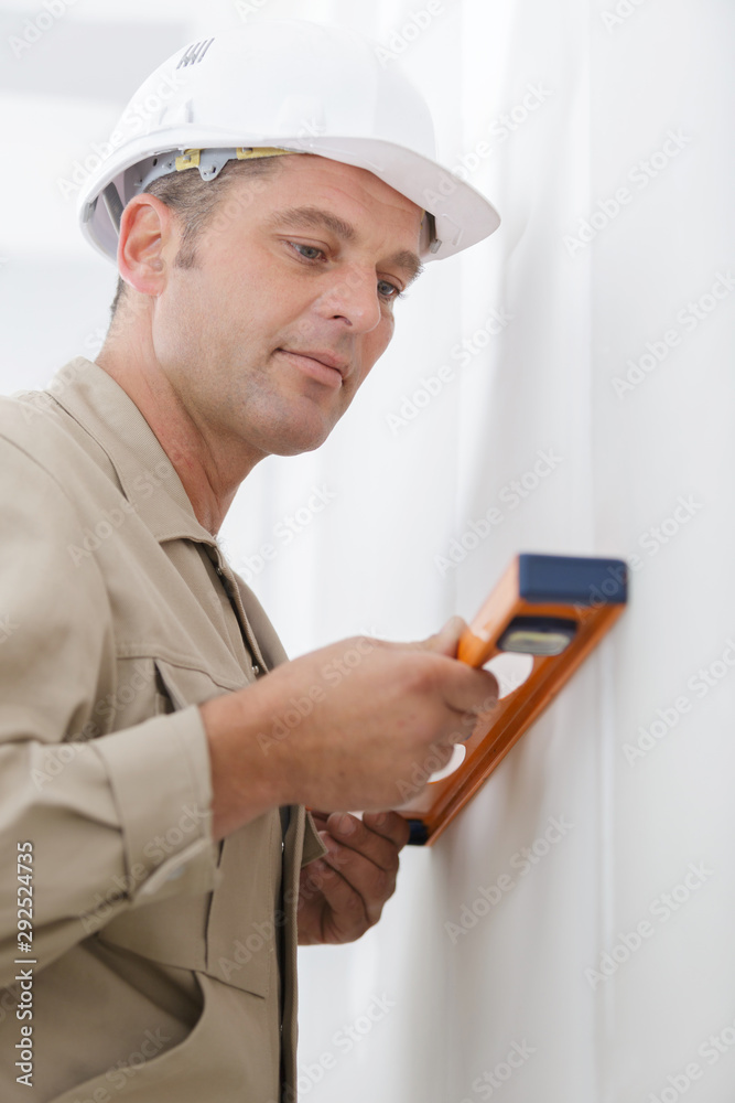 professional worker in helmet is measuring wall with level professional worker in helmet is measuring wall with level