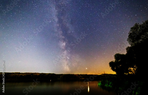 The stars and the milky way are reflected in the river.