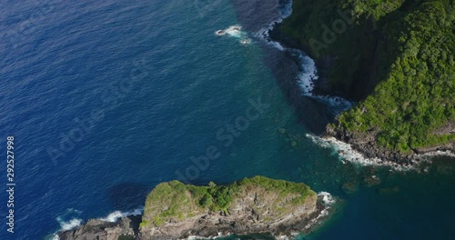 Aerial view flying over smally sunny uninhabited island near a lush green coastline with deep blue ocean water, jurassic coastlines photo