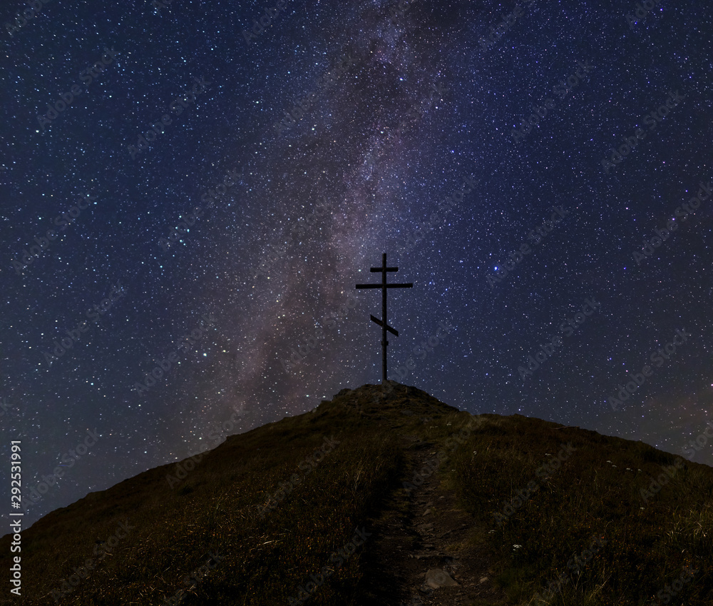 night scene, christian cross on a top of grass hill under a starry sky with milky way