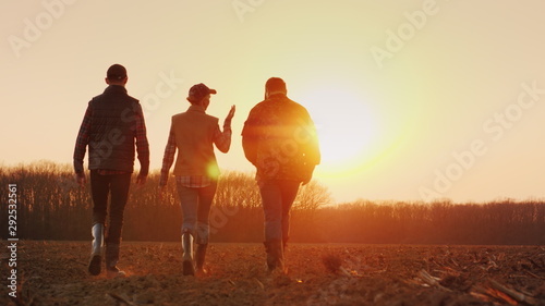 Obraz na płótnie Three farmers go ahead on a plowed field at sunset