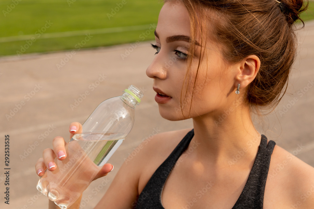 Young sexy athletic girl drinks water, standing on a stadium. Young sexy athletic girl drinks water, standing on a stadium.